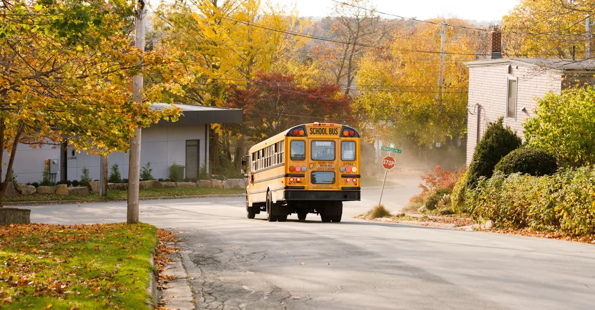 A yellow school bus on a village road during a crisp autumn day, surrounded by colorful trees.